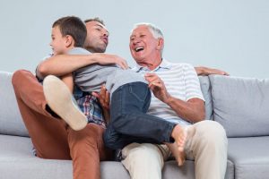 Father sitting on sofa with grandfather and embracing son in liv