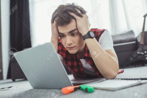 stressed teen boy studying with laptop while lying on floor