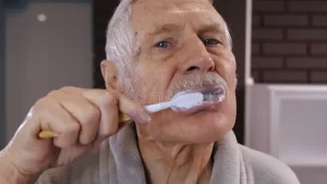 abuelo-anciano-con-dientes-de-lavado-albornoz-mirando-al-espejo-higiene-matutina-en-el-baño-alegre-y-un-hermoso-haciendo-después-202141892